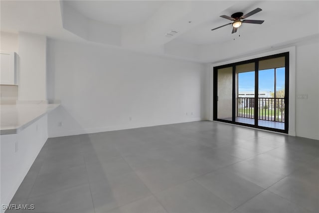 tiled empty room with a raised ceiling and ceiling fan