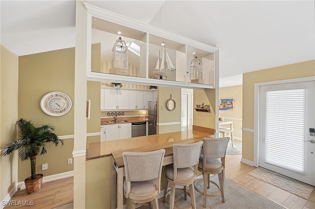 kitchen with stainless steel appliances, kitchen peninsula, sink, white cabinetry, and light hardwood / wood-style flooring