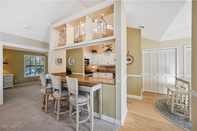 kitchen featuring light hardwood / wood-style floors, kitchen peninsula, a breakfast bar area, white cabinetry, and appliances with stainless steel finishes