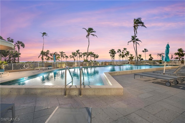 pool at dusk with a water view and a patio