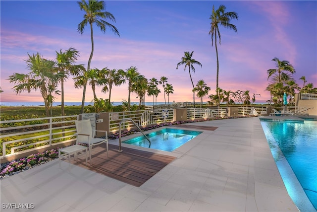 pool at dusk featuring a jacuzzi