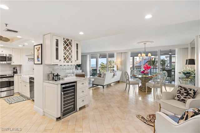 kitchen featuring white cabinetry, appliances with stainless steel finishes, decorative backsplash, an inviting chandelier, and beverage cooler