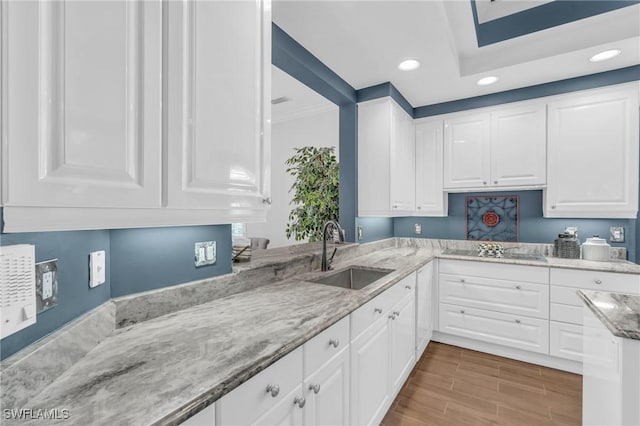 kitchen featuring wood finish floors, white cabinetry, a sink, and light stone countertops