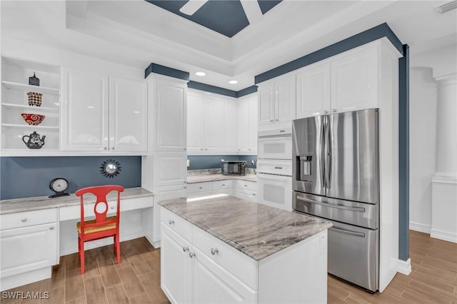 kitchen featuring built in study area, stainless steel fridge with ice dispenser, light stone counters, wood tiled floor, and white cabinetry