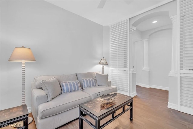 living room featuring baseboards, wood finished floors, a ceiling fan, and ornate columns