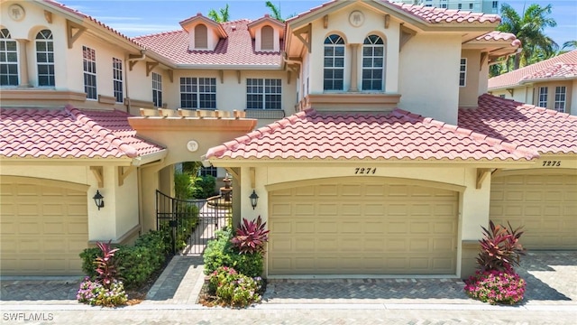 mediterranean / spanish-style house featuring a garage, a tile roof, a gate, and stucco siding