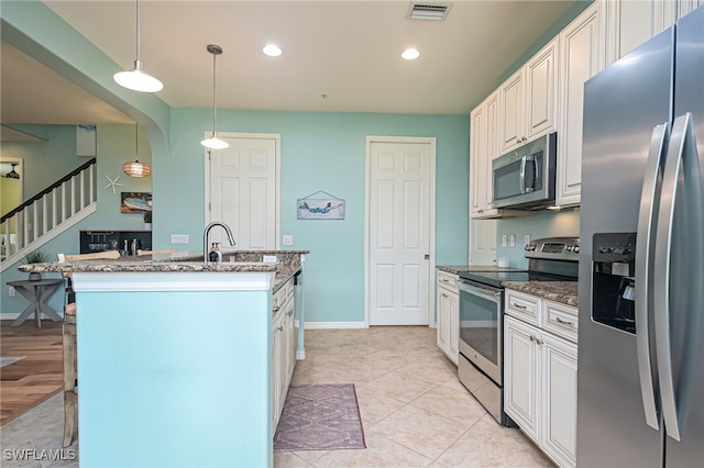 kitchen with dark stone counters, white cabinetry, stainless steel appliances, and decorative light fixtures