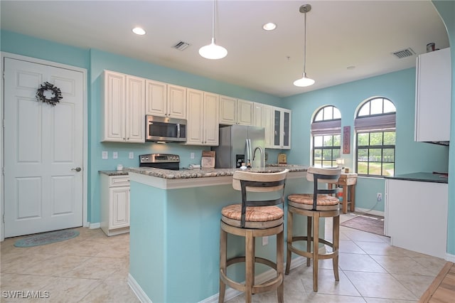 kitchen with light stone countertops, stainless steel appliances, decorative light fixtures, a kitchen island with sink, and a breakfast bar