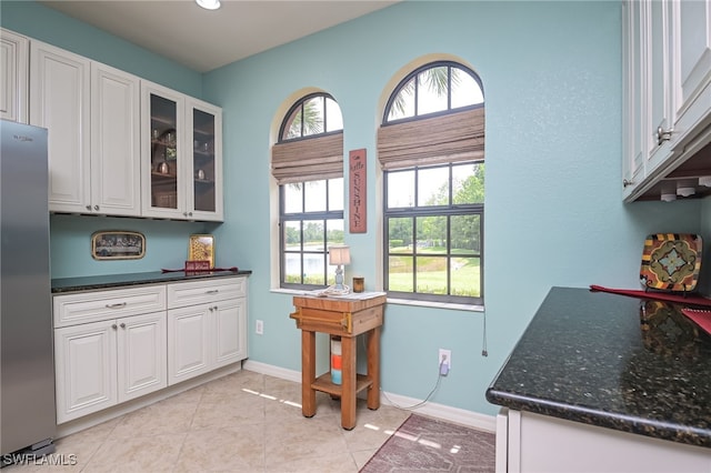 kitchen featuring stainless steel fridge, light tile patterned floors, white cabinetry, and dark stone countertops