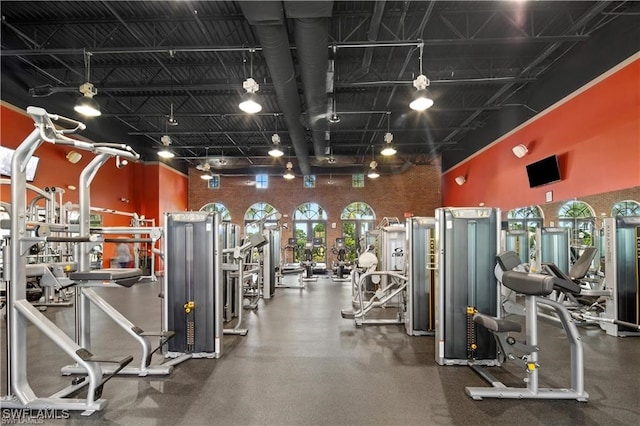 exercise room featuring a towering ceiling, track lighting, and a healthy amount of sunlight