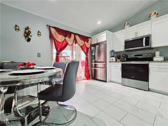 kitchen with stainless steel appliances, light stone countertops, white cabinetry, and vaulted ceiling