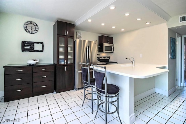 kitchen featuring a peninsula, a kitchen breakfast bar, light countertops, appliances with stainless steel finishes, and glass insert cabinets