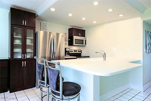 kitchen featuring a kitchen bar, kitchen peninsula, stainless steel appliances, sink, and light tile patterned floors