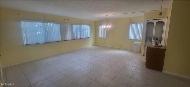 unfurnished room with a wealth of natural light, light tile patterned floors, and an inviting chandelier