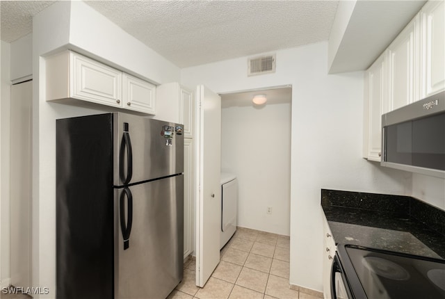 kitchen featuring stainless steel appliances, white cabinets, light tile patterned flooring, washer / clothes dryer, and dark stone countertops