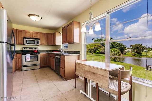 kitchen featuring stainless steel appliances, sink, light tile patterned floors, decorative light fixtures, and a water view