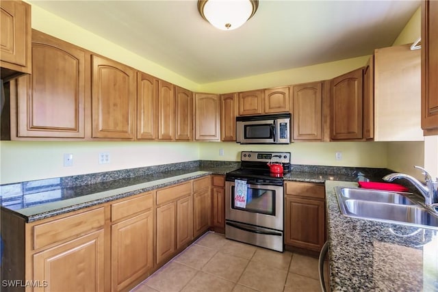 kitchen with light tile patterned floors, sink, appliances with stainless steel finishes, and dark stone counters