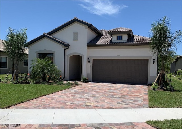 mediterranean / spanish-style home featuring a tiled roof, an attached garage, decorative driveway, a front lawn, and stucco siding