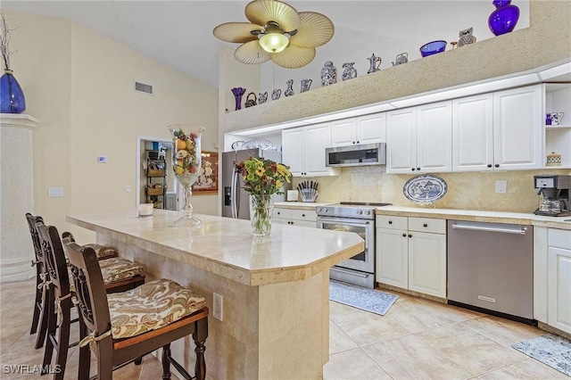 kitchen featuring high vaulted ceiling, white cabinets, a kitchen bar, kitchen peninsula, and stainless steel appliances