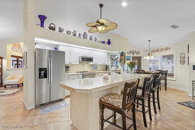 kitchen with light tile patterned floors, high vaulted ceiling, a kitchen bar, white cabinets, and appliances with stainless steel finishes