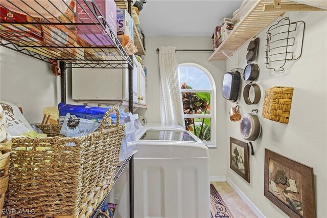 laundry area featuring washing machine and clothes dryer, light tile patterned floors, and cabinets