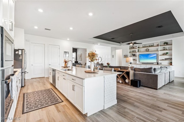 kitchen featuring sink, a tray ceiling, stainless steel appliances, a kitchen island with sink, and white cabinets