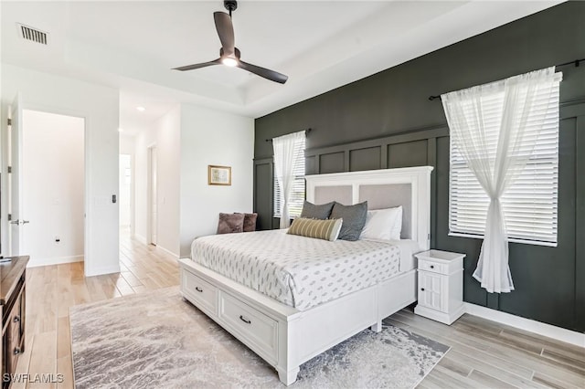 bedroom featuring ceiling fan, a tray ceiling, and light wood-type flooring