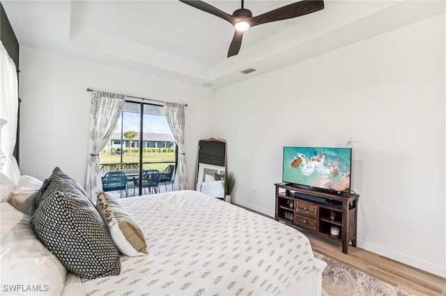 bedroom with a raised ceiling, hardwood / wood-style flooring, access to outside, and ceiling fan