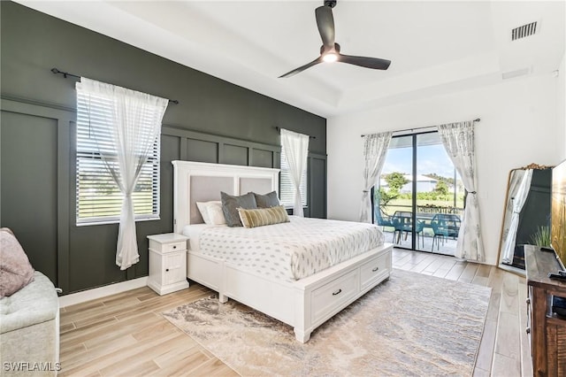 bedroom featuring ceiling fan, access to exterior, light hardwood / wood-style floors, and a tray ceiling