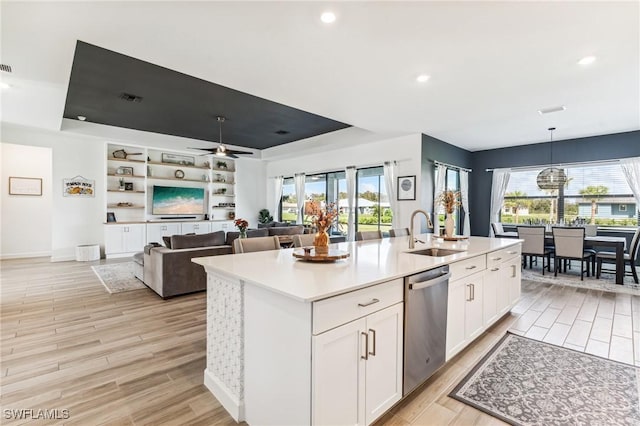 kitchen featuring decorative light fixtures, white cabinetry, dishwasher, sink, and an island with sink