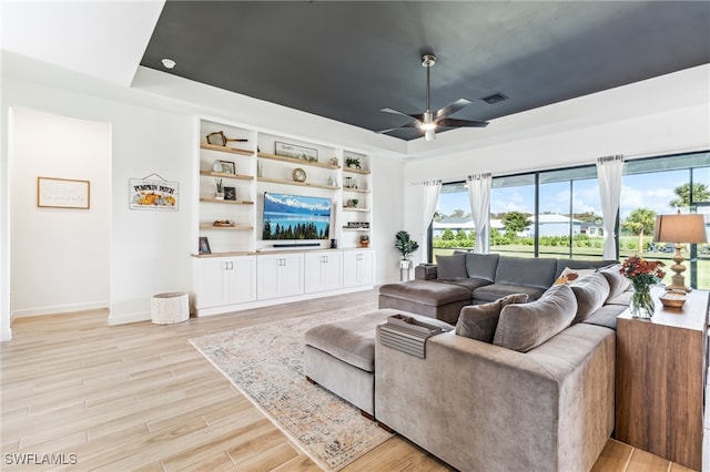 living room with ceiling fan, a raised ceiling, and light hardwood / wood-style floors