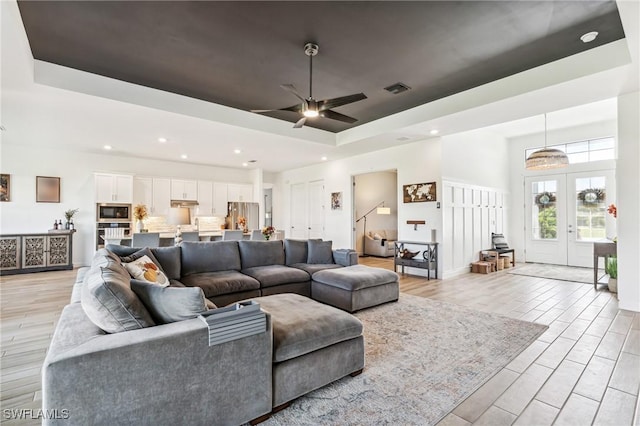 living room featuring french doors, light hardwood / wood-style flooring, ceiling fan, and a tray ceiling