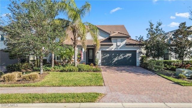 mediterranean / spanish-style house featuring a tile roof, stucco siding, a front lawn, decorative driveway, and a garage
