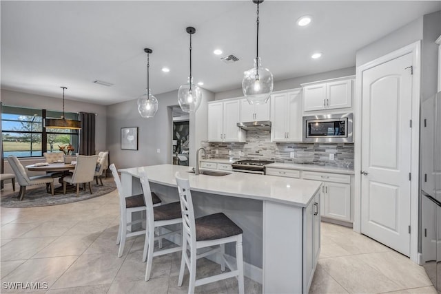 kitchen with a kitchen island with sink, stainless steel appliances, hanging light fixtures, white cabinets, and sink