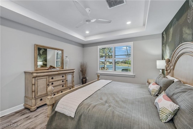 bedroom with ceiling fan, a tray ceiling, and light hardwood / wood-style floors