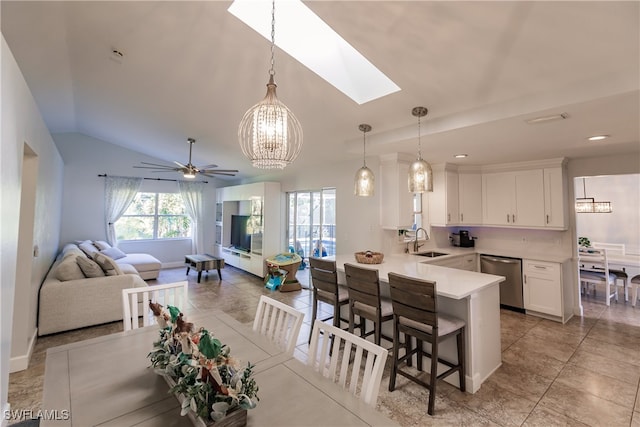 kitchen featuring pendant lighting, dishwasher, lofted ceiling with skylight, sink, and white cabinetry