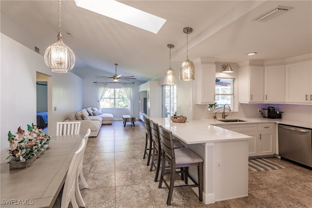 kitchen featuring dishwasher, lofted ceiling with skylight, decorative light fixtures, a kitchen bar, and white cabinetry