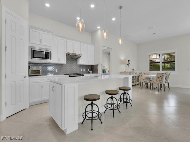 kitchen with white cabinetry, stainless steel microwave, an island with sink, and pendant lighting