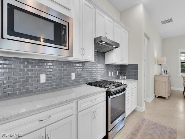 kitchen with white cabinetry, appliances with stainless steel finishes, light tile patterned floors, backsplash, and light stone counters