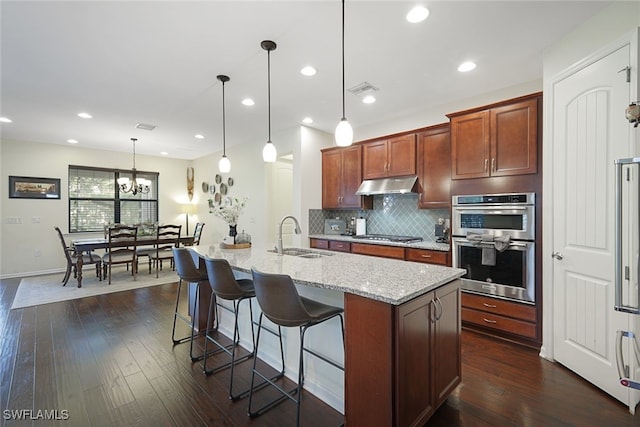 kitchen featuring hanging light fixtures, sink, an island with sink, and dark hardwood / wood-style floors