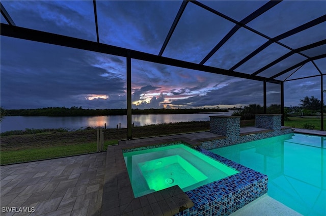 pool at dusk featuring a patio, glass enclosure, an in ground hot tub, and a water view