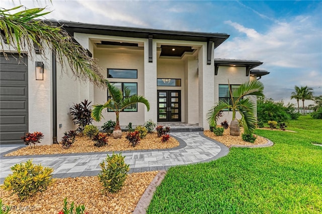 view of exterior entry featuring a garage, a lawn, and french doors