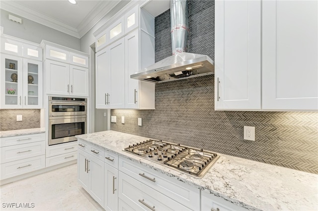 kitchen featuring light stone counters, decorative backsplash, wall chimney range hood, white cabinetry, and appliances with stainless steel finishes