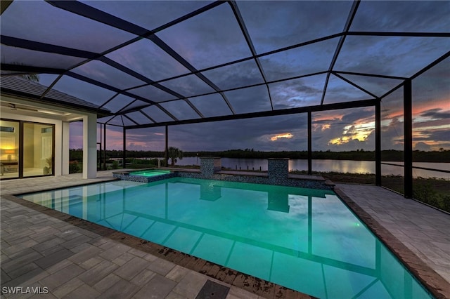 pool at dusk with a patio, a water view, a lanai, and an in ground hot tub