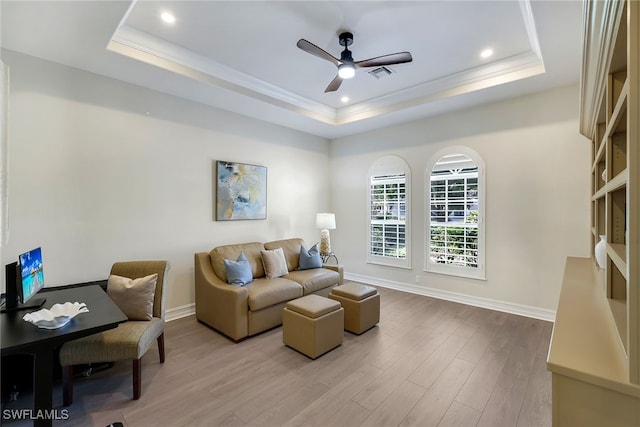 living room with a raised ceiling, ceiling fan, and light hardwood / wood-style flooring