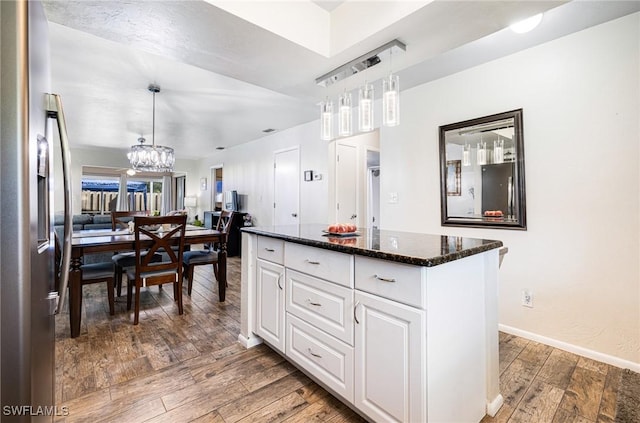 kitchen with hardwood / wood-style floors, stainless steel fridge, dark stone countertops, pendant lighting, and white cabinets