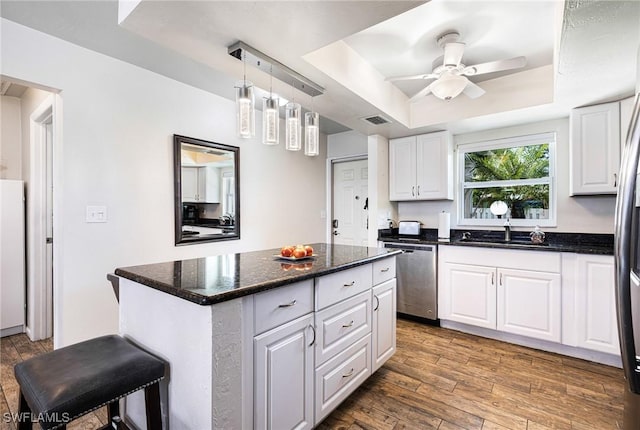 kitchen featuring ceiling fan, a center island, a tray ceiling, appliances with stainless steel finishes, and white cabinets