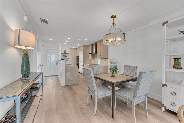 dining space with crown molding, sink, a chandelier, and light wood-type flooring