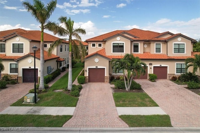 mediterranean / spanish house with stone siding, stucco siding, a tile roof, and decorative driveway