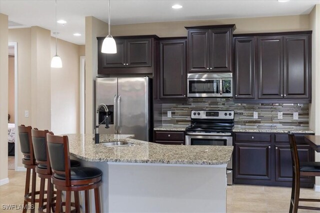 kitchen with a center island with sink, stainless steel appliances, backsplash, and decorative light fixtures